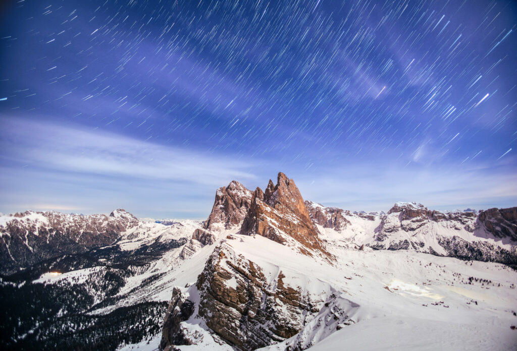 A landscape photograph of the Seceda Ridgeline in Italy, photographed to include star trails at night.